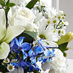 ورود بيضاء وزرقاء في مزهرية زجاجية مربعة الشكل
