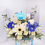 باقة ورد أبيض وأزرق في إناء مربع مكتوب عليه إنه صبي