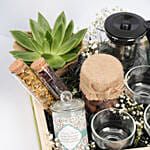 سلة خشبية فيها أبريق وأكواب شاي وكوكيز وشمعة وصبار والمزيد